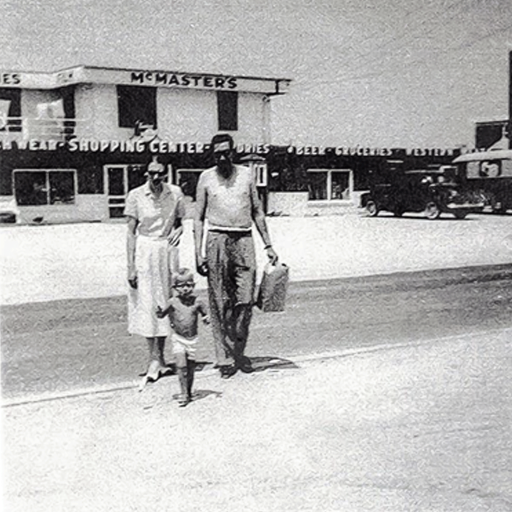 metz original founders in a grainy photo, walking towards the beach with their shopping center behind them.